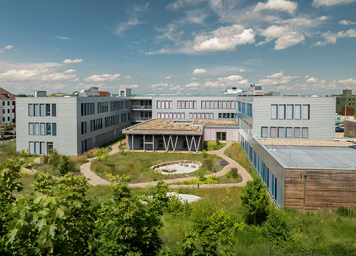 Rückansicht des modularen Bürogebäudes mit begrünter Außenanlage, Innenhof und eingeschossigem Pavillon in Holzbauweise. Bild: Kleusberg