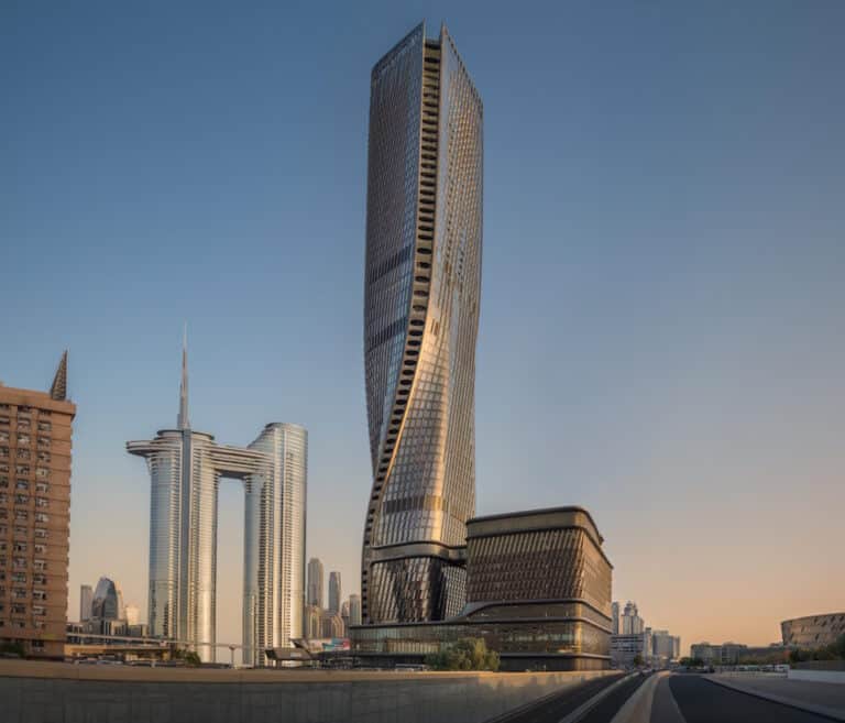 Twisting high-rise dominates Dubai-like skyline with a highway in the foreground and other modern towers at sunset/overtime light.