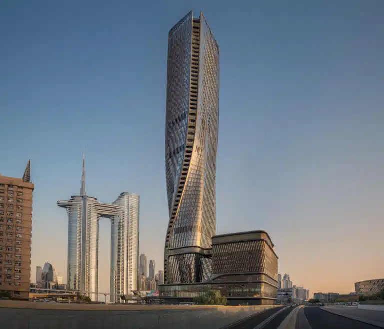Twisting high-rise dominates Dubai-like skyline with a highway in the foreground and other modern towers at sunset/overtime light.