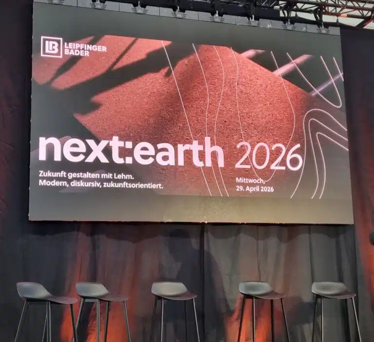 Large stage screen reading 'next:earth 2026' with a red textured background, logo top-left, and five stools below.
