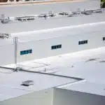 Aerial view of flat white factory rooftops with vents, skylights, and metal equipment fixtures scattered across the surface.