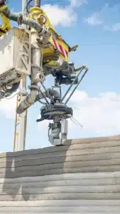 Heavy construction machinery with a yellow attachment pours or places concrete onto a wall under a clear blue sky