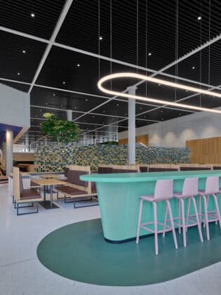 Contemporary open‑plan lounge with a turquoise curved bar, pink stools, and wooden tables under a black grid ceiling.