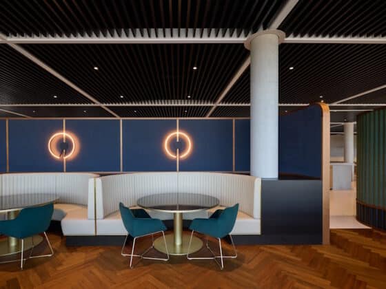 Modern lounge seating with white curved booths, teal chairs, and round tables beneath circular wall lights on a blue panel wall.