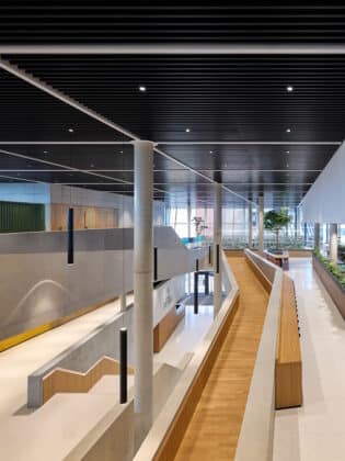 Modern multi-level interior with curved wooden seating, concrete columns, and bright walkways in a contemporary building atrium