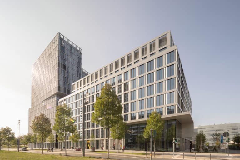 Modern glass office building with trees along a street in daylight.