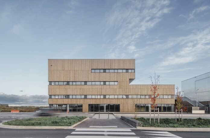 Contemporary wood-clad office building with long horizontal windows and a glass storefront beneath a blue sky