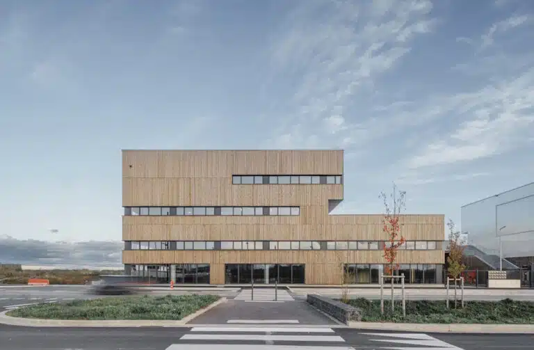 Contemporary wood-clad office building with long horizontal windows and a glass storefront beneath a blue sky