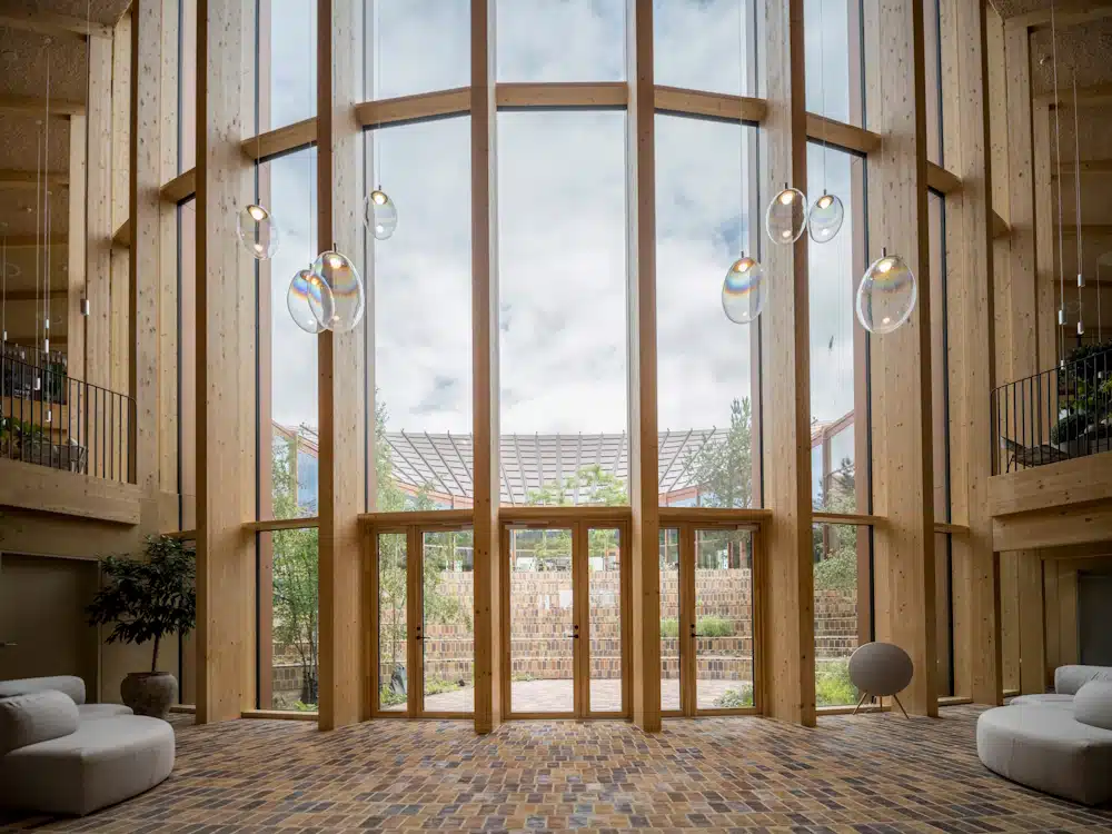 Tall wooden atrium with floor-to-ceiling windows, hanging glass pendant lights, and a brick courtyard visible outside