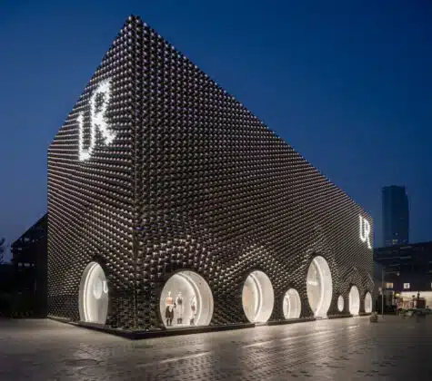 Night view of a futuristic building with a dark bubbled facade and circular, illuminated doorways along its side.