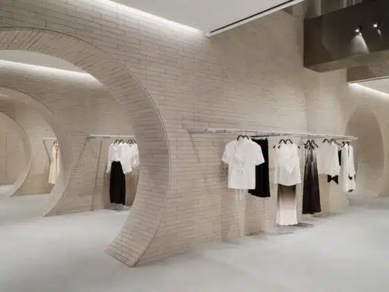 Minimalist clothing store with beige brick circular arches and racks of white and neutral-toned garments on display.