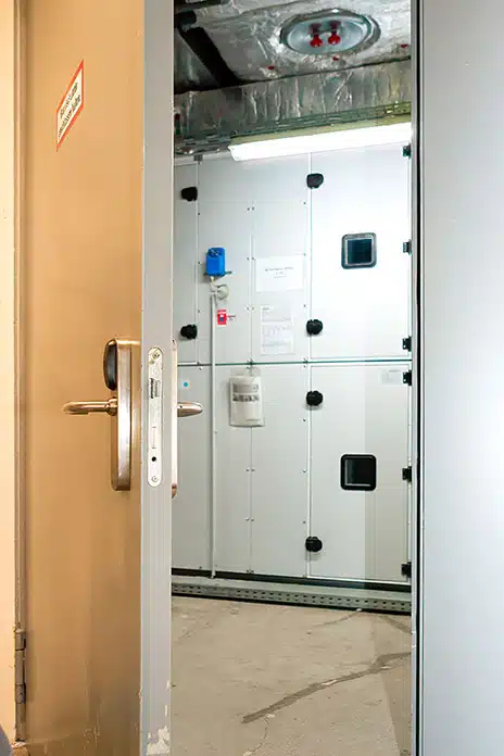 Geöffnete Tür mit elektronischem Zutrittsleser vor einem technischen Raum mit Schaltschränken.